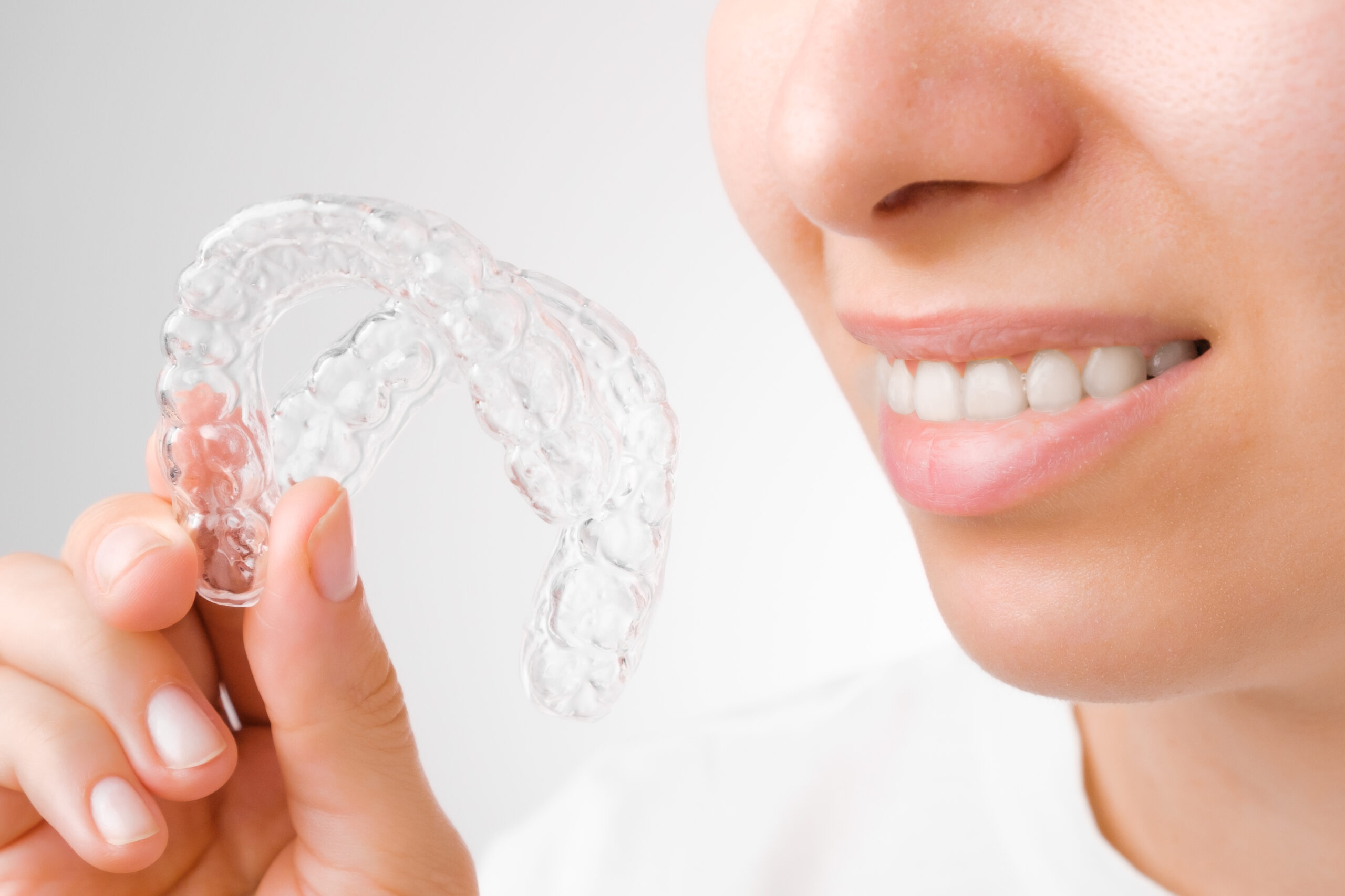 Cheerful young woman holding plastic transparent braces. Orthodontic silicone aligner for whitening and straightening.